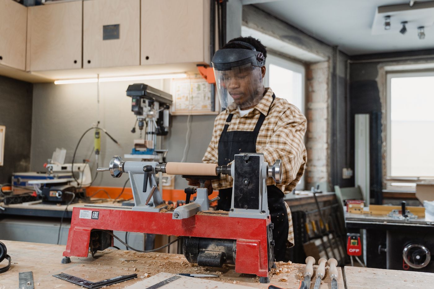 An artisan concentrates on work at a wood lathe in a well-lit workshop