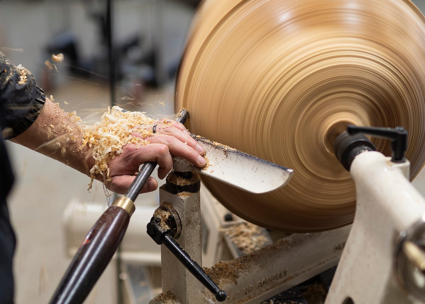 A woodturner shaping the outside of a wooden bowl on a lathe