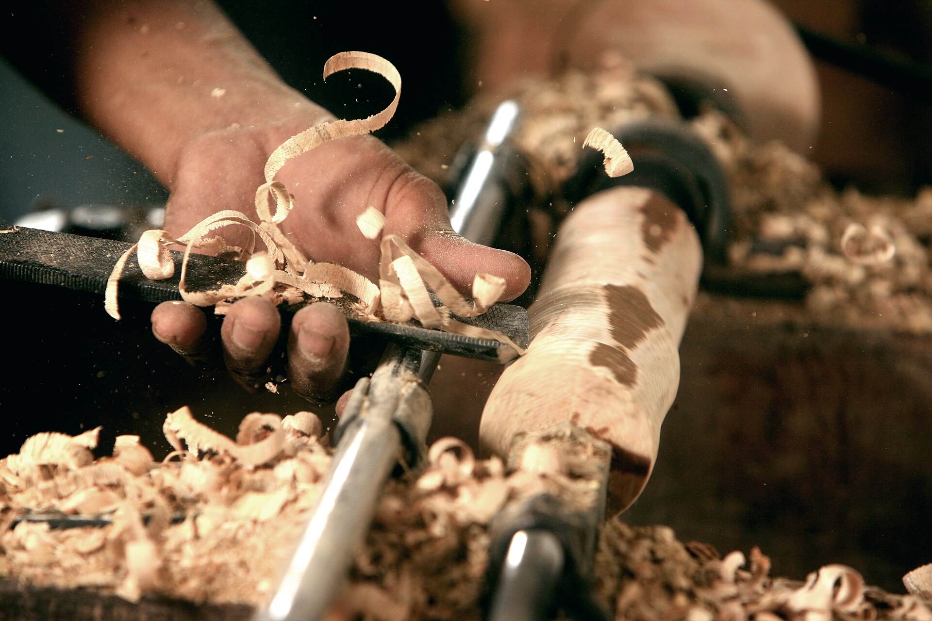A woodturner making a cut on a mounted bowl blank, long shavings curling off the gouge
