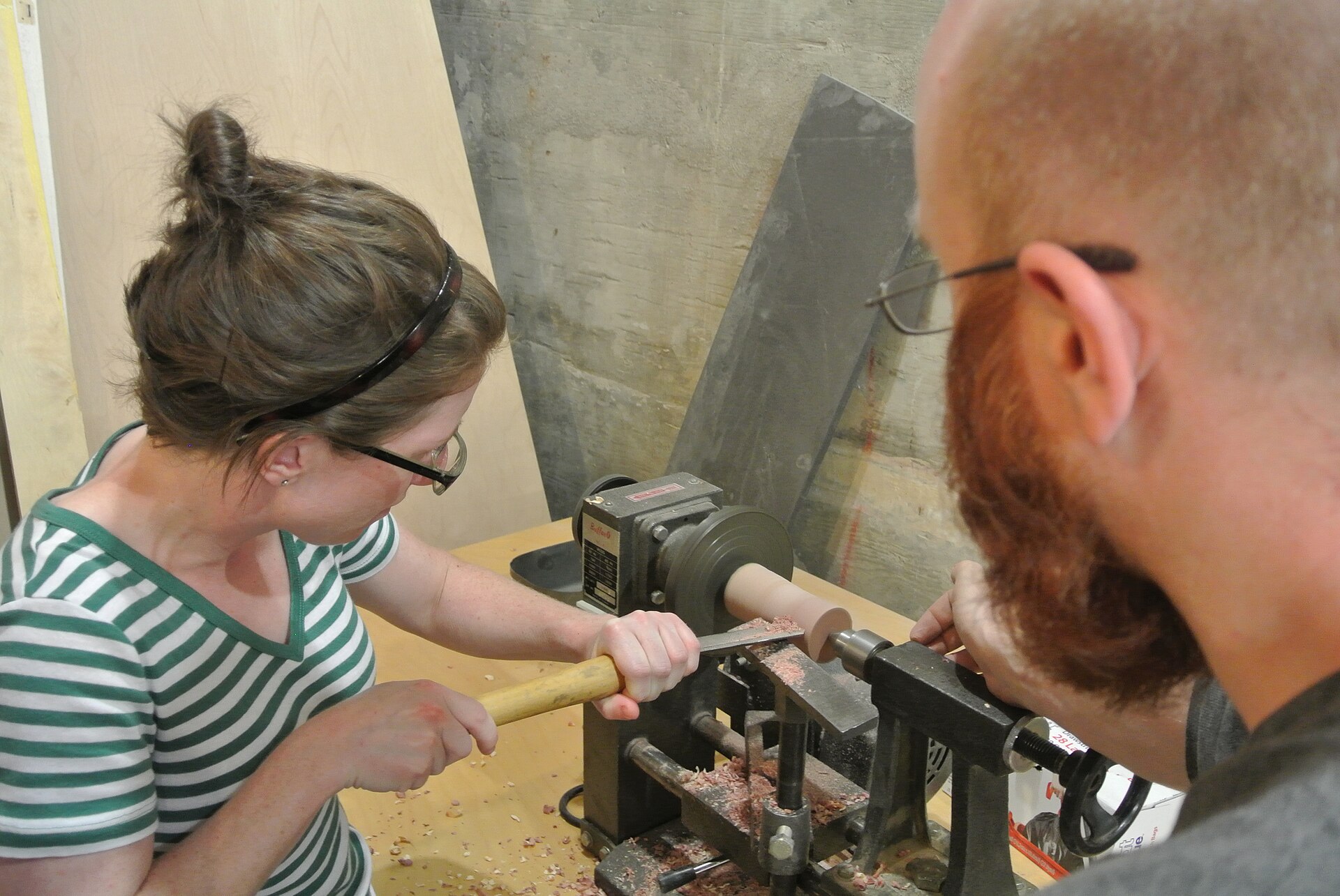 A woodturner at a lathe with shavings accumulating on the floor and tool rest visible
