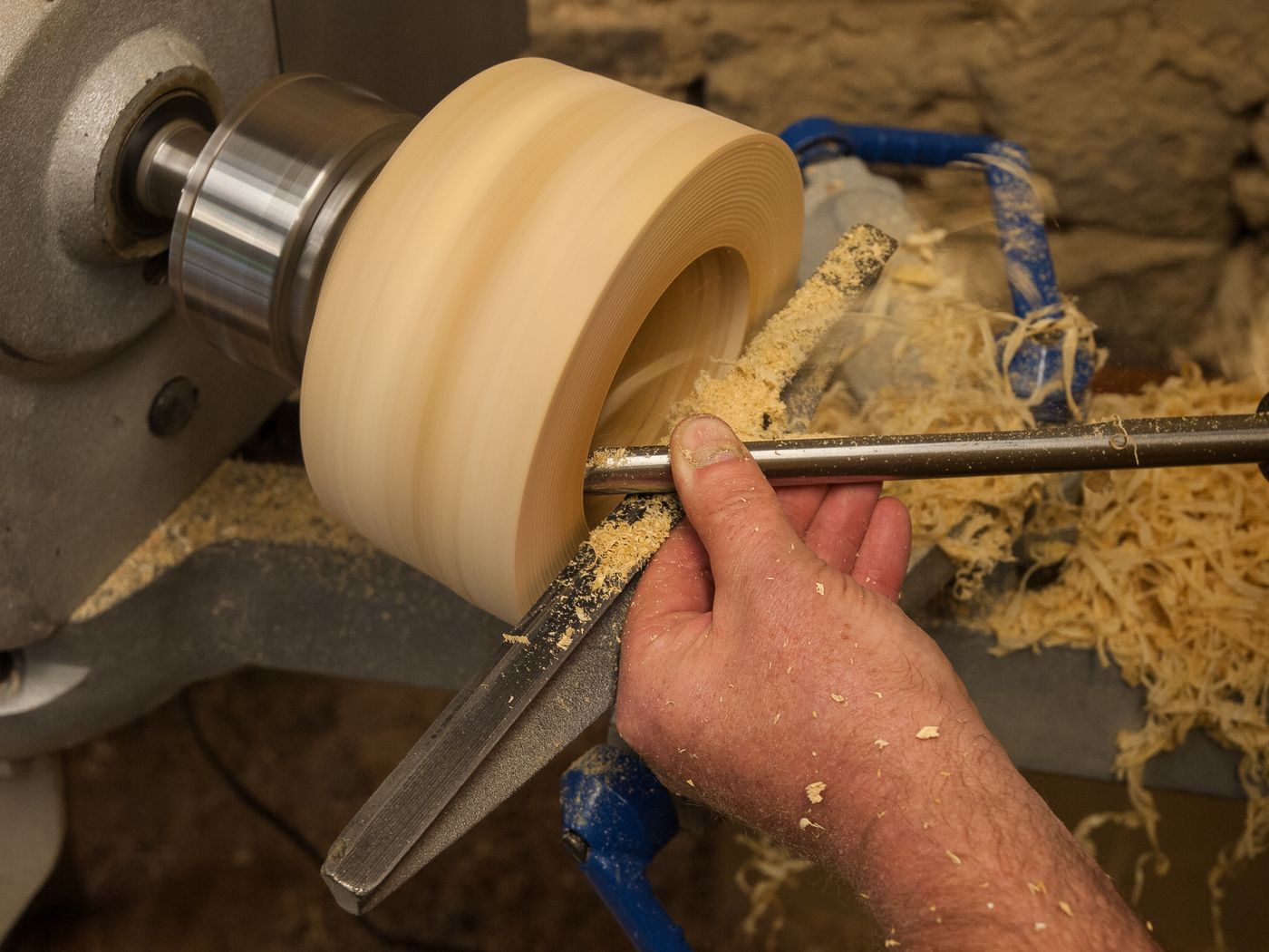 A woodturner concentrates on work at a lathe, workshop tools visible in the background