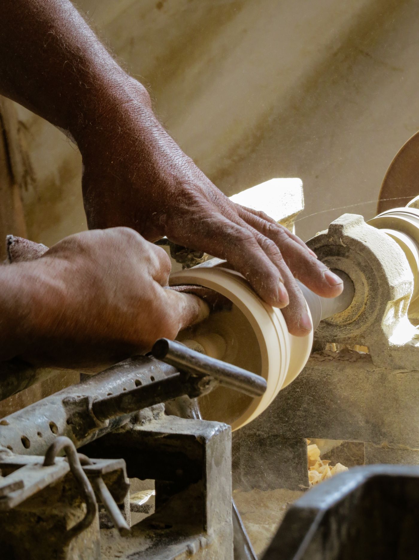 Close-up detail of a woodturner's hands and turning tool at the lathe