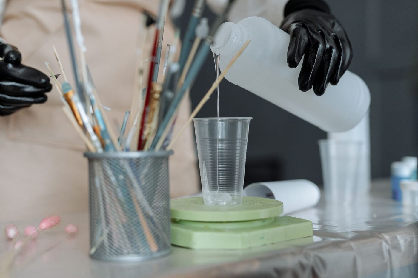 A gloved hand pouring resin into a container, the kind of PPE used when handling stabilizing resin