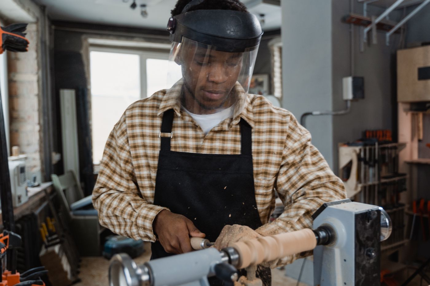 A turner focuses on shaping a piece on a lathe, the workshop behind showing tools and equipment
